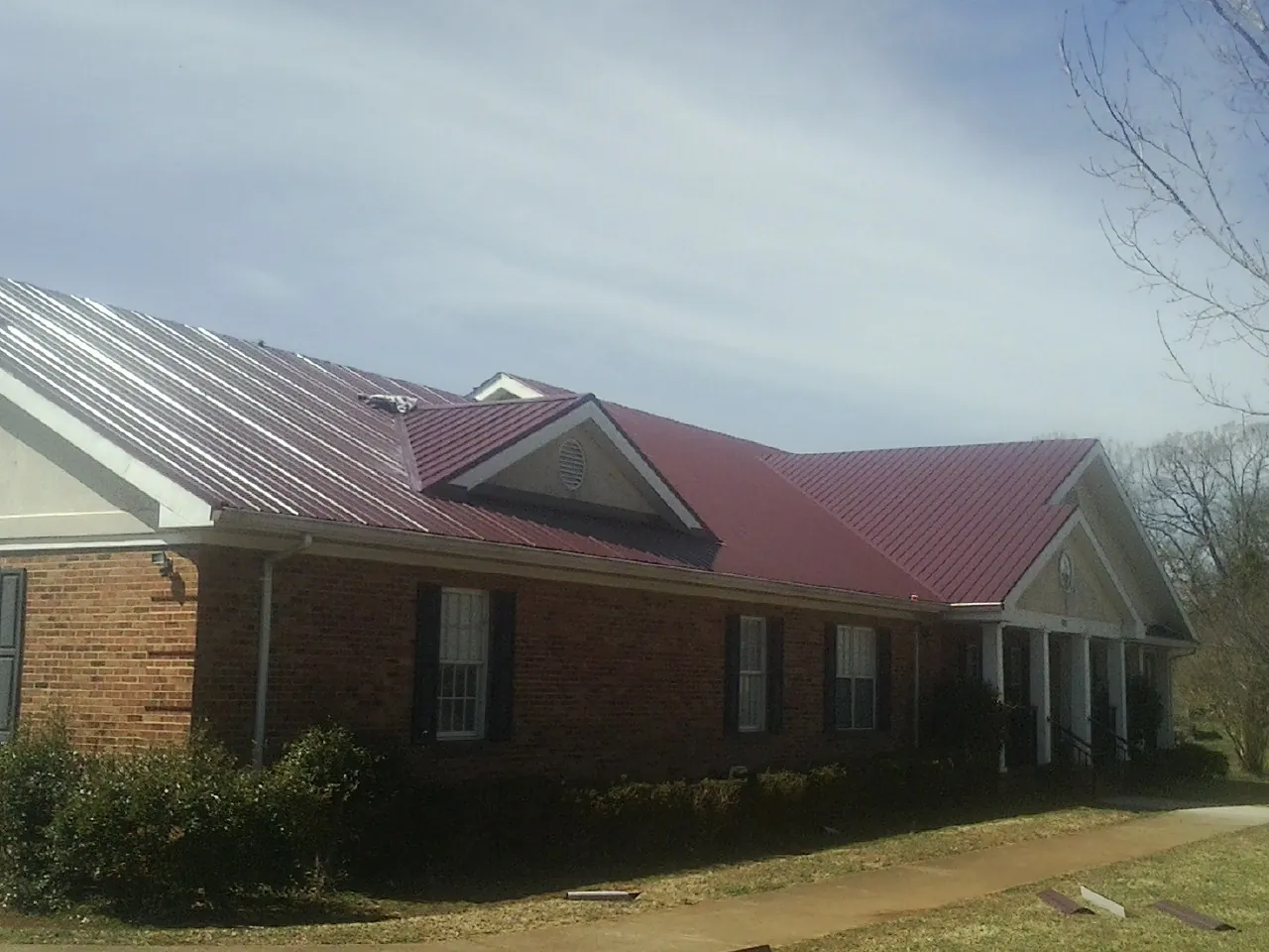 Red metal roof with gabled entries on a long brick building, from a Hail Damage Roof Repair job in Brogue