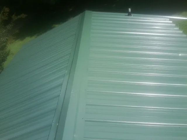 New green metal panels meeting at the ridge of a roof — Flat Roof Repair work by our crew in Brogue