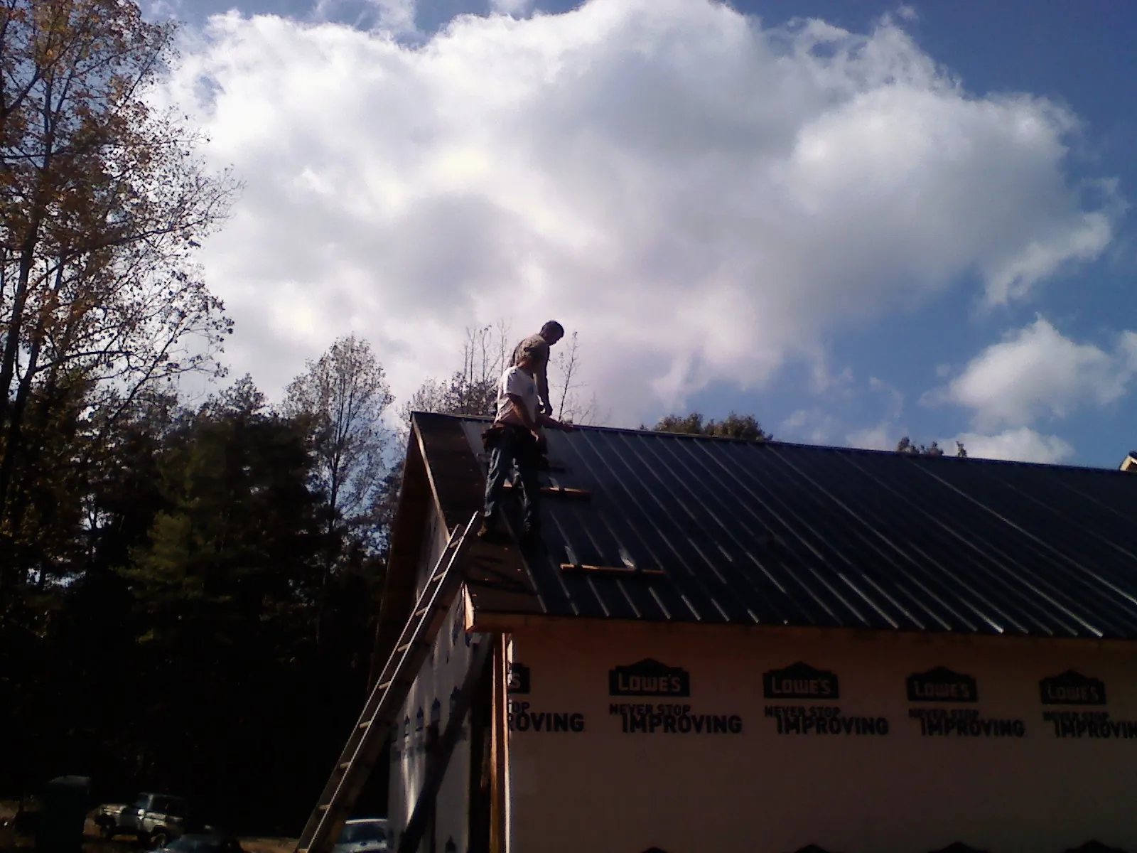 Roofer fastening dark metal panels high against a cloudy sky, from a Roof Inspection job in Brogue