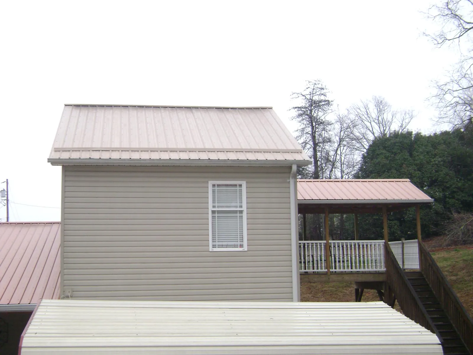 Tan metal roofs on a two story addition and attached porch, from a Roof Replacement job in Brogue